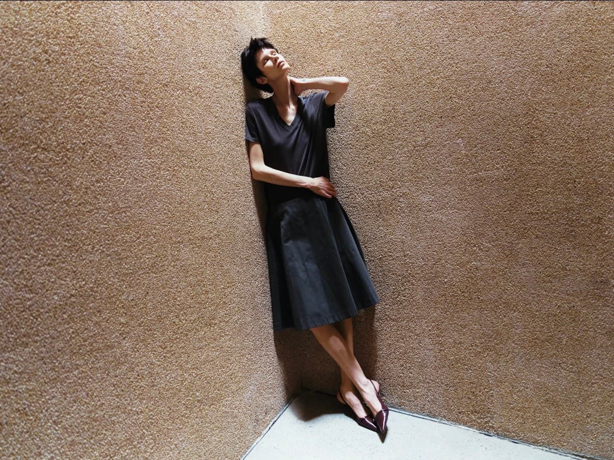 Gentle Authority figure in black dress leaning against a wall