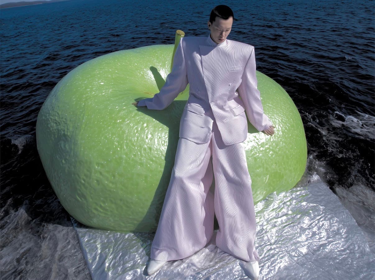 Model leaning against a giant green apple by the water