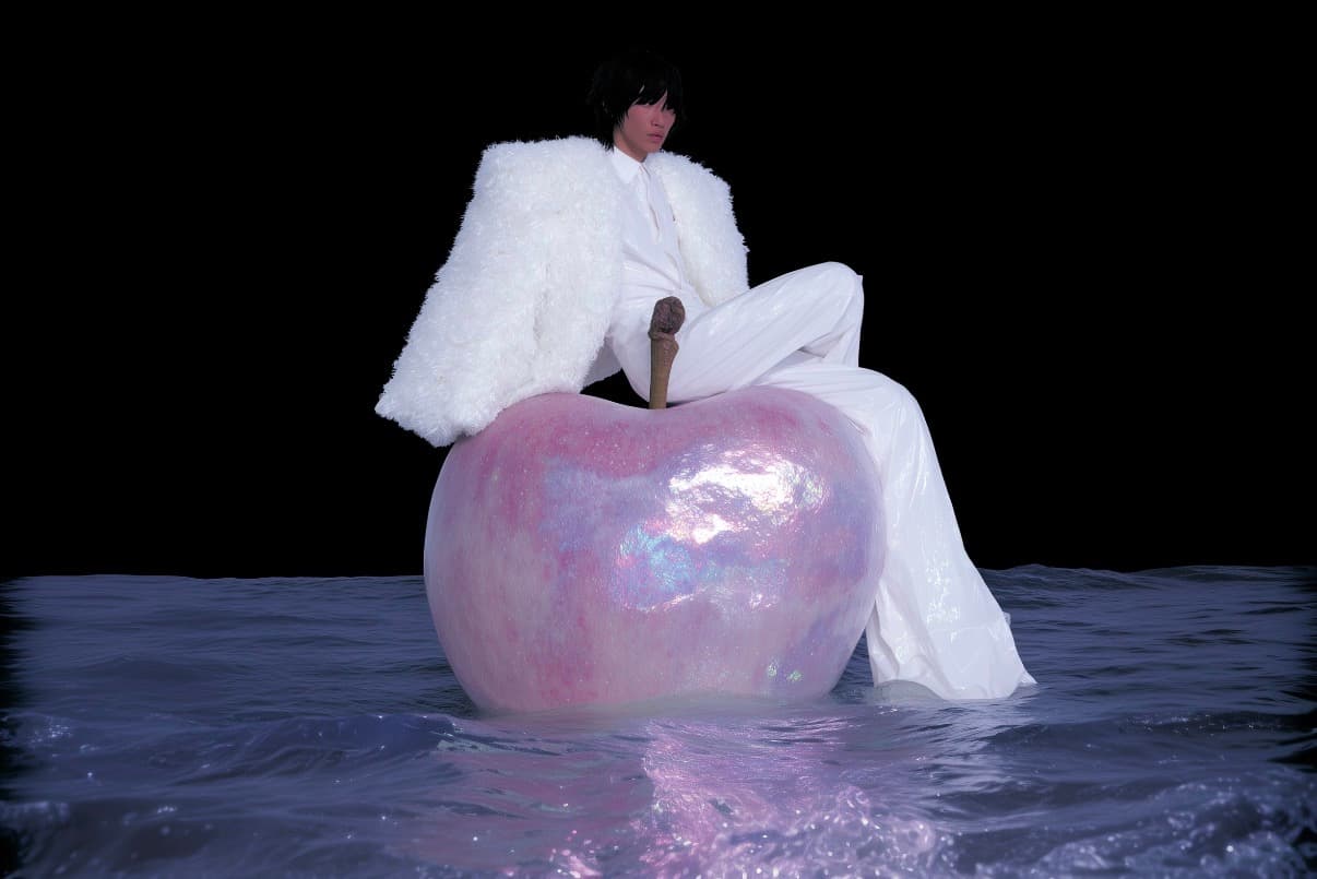 Model sitting on a pearlescent apple in a dark dream space